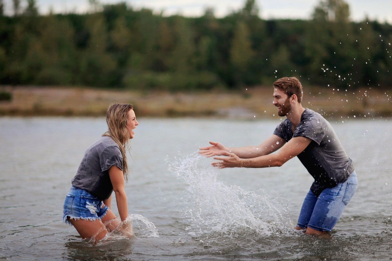Homem e mulher brincando em um rio, jogando água um no outro.