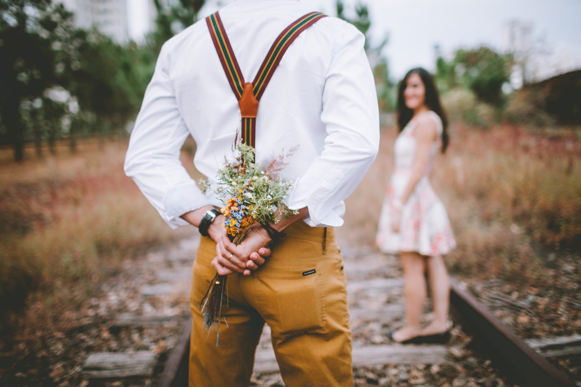 Foto de homem segurando buque de flores e mulher olhando pra ele