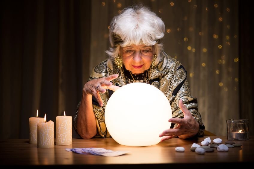 Mulher idosa em mesa com cartas de tarot, velas, cristais e bola de Cristal