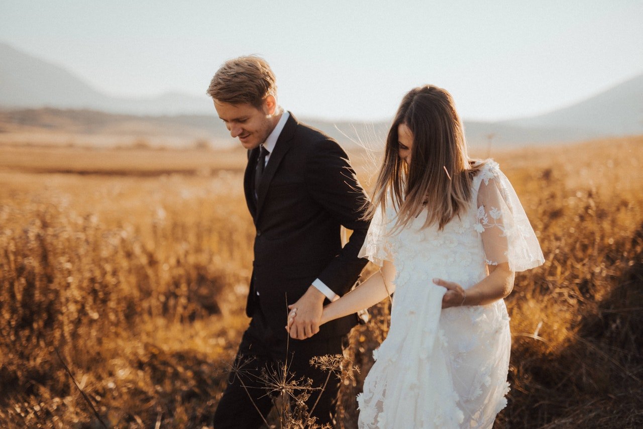 Homem e mulher com vestes de casamento andando em um campo de trigo.