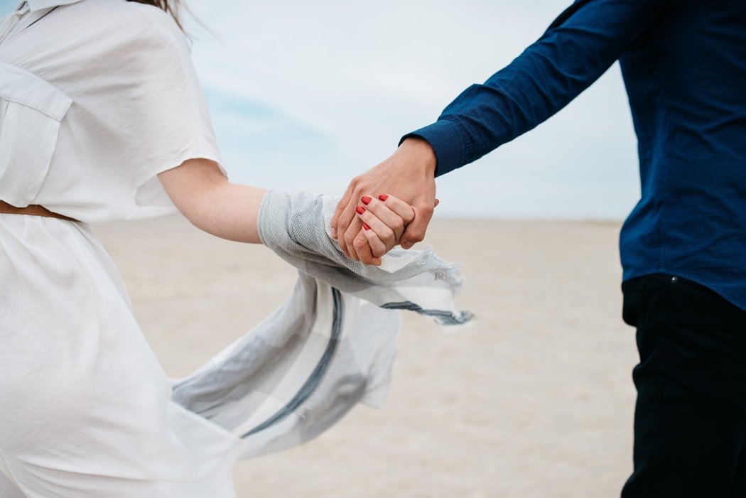 Mulher e homem de mãos dadas em uma praia. A foto só mostra o centro de seus corpos.