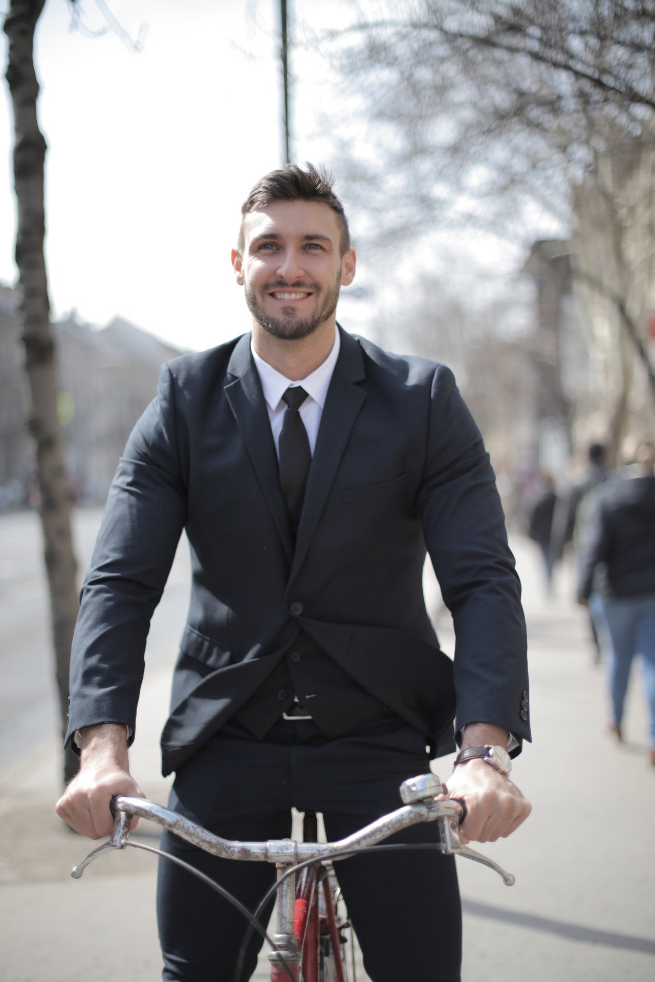 Homem de terno e gravata andando de bicicleta ao ar livre, enquanto sorri.