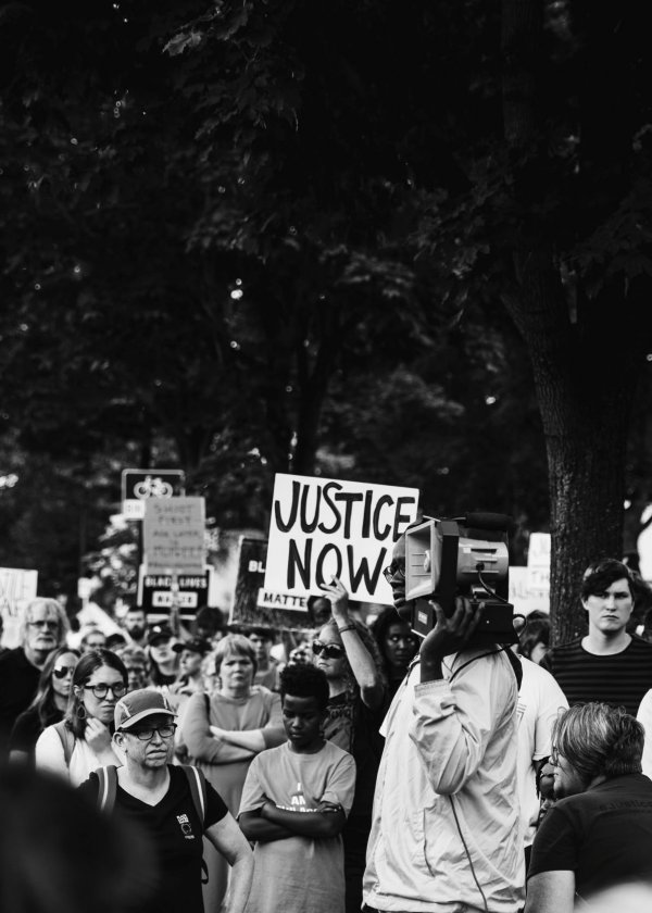 Unsplash/Isaiah Rustad Cartaz com os escritos 'justiça agora' levantado em protesto de rua.