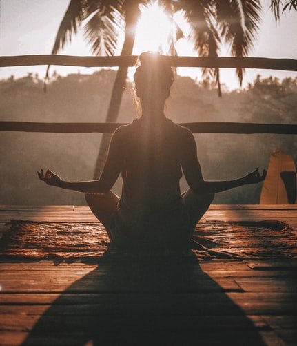 Menina sentada praticando Yoga em varanda durante pôr do Sol