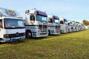 Needpix - reverent (pixabay.com) Doze caminhões de circo estacionados lado a lado.