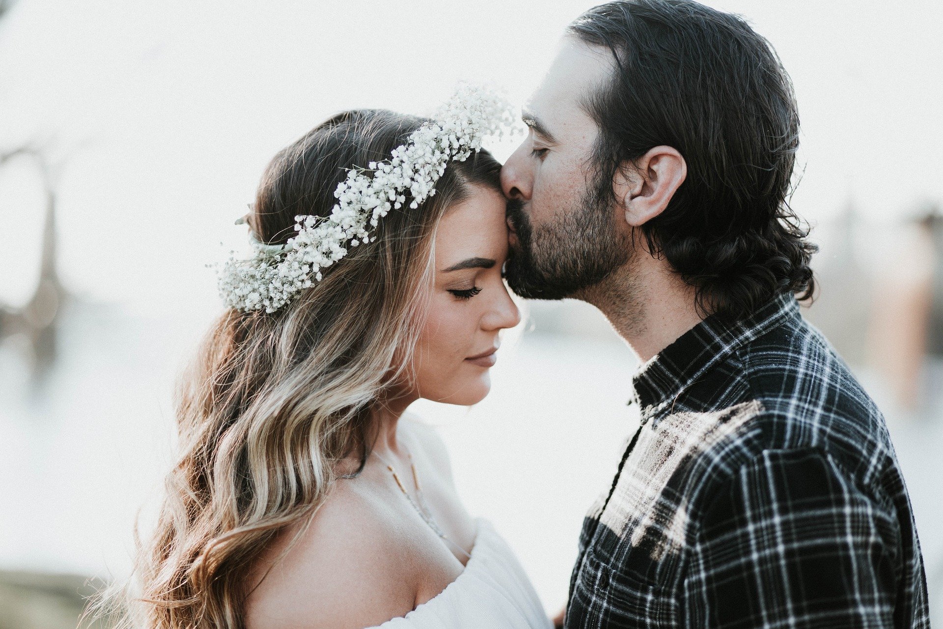 Homem beijando testa de mulher que está vestida de noiva