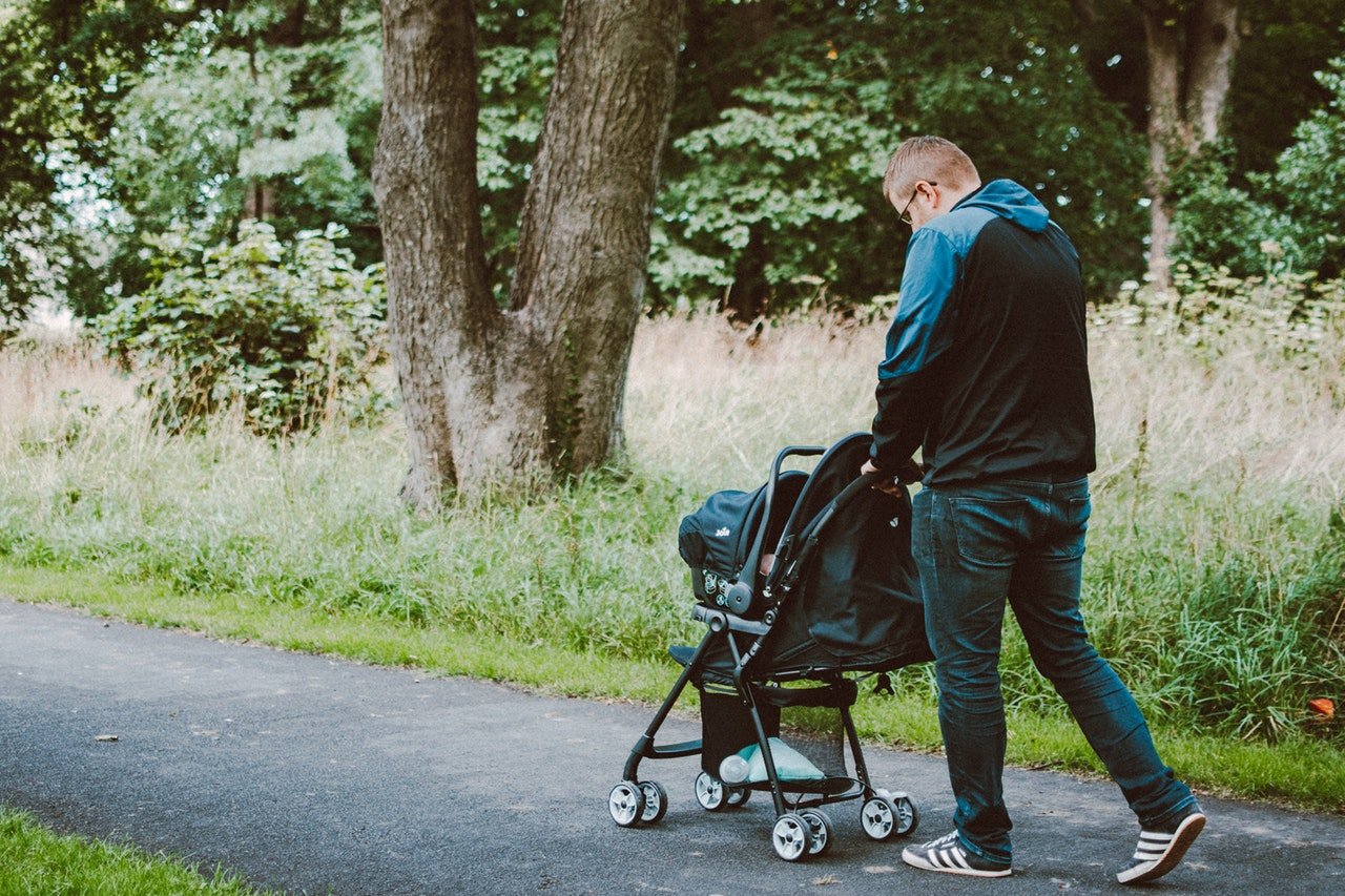 Homem passeando com carrinho de bebê em parque.