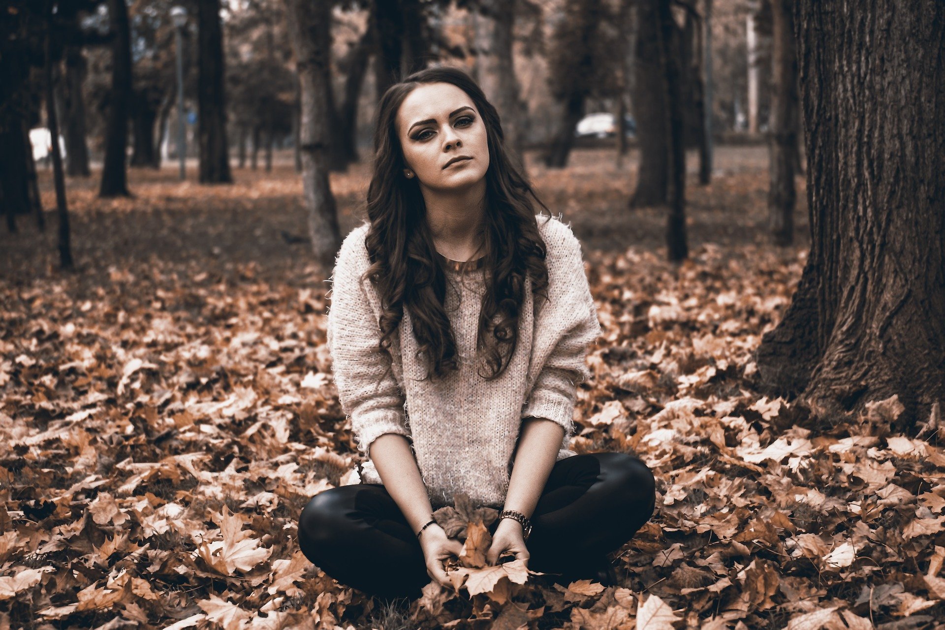 Mulher sentada em floresta de folhas secas, com expressão séria