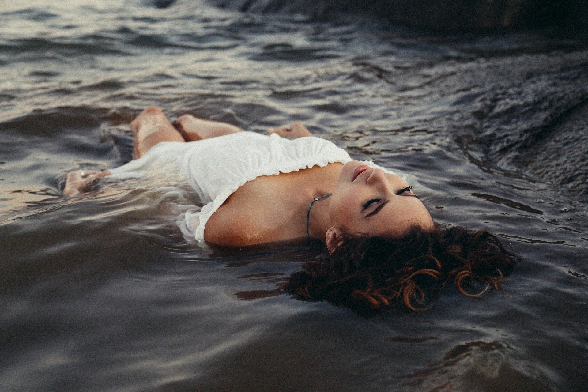 Mulher deitada em águas de rio, olhando para o céu