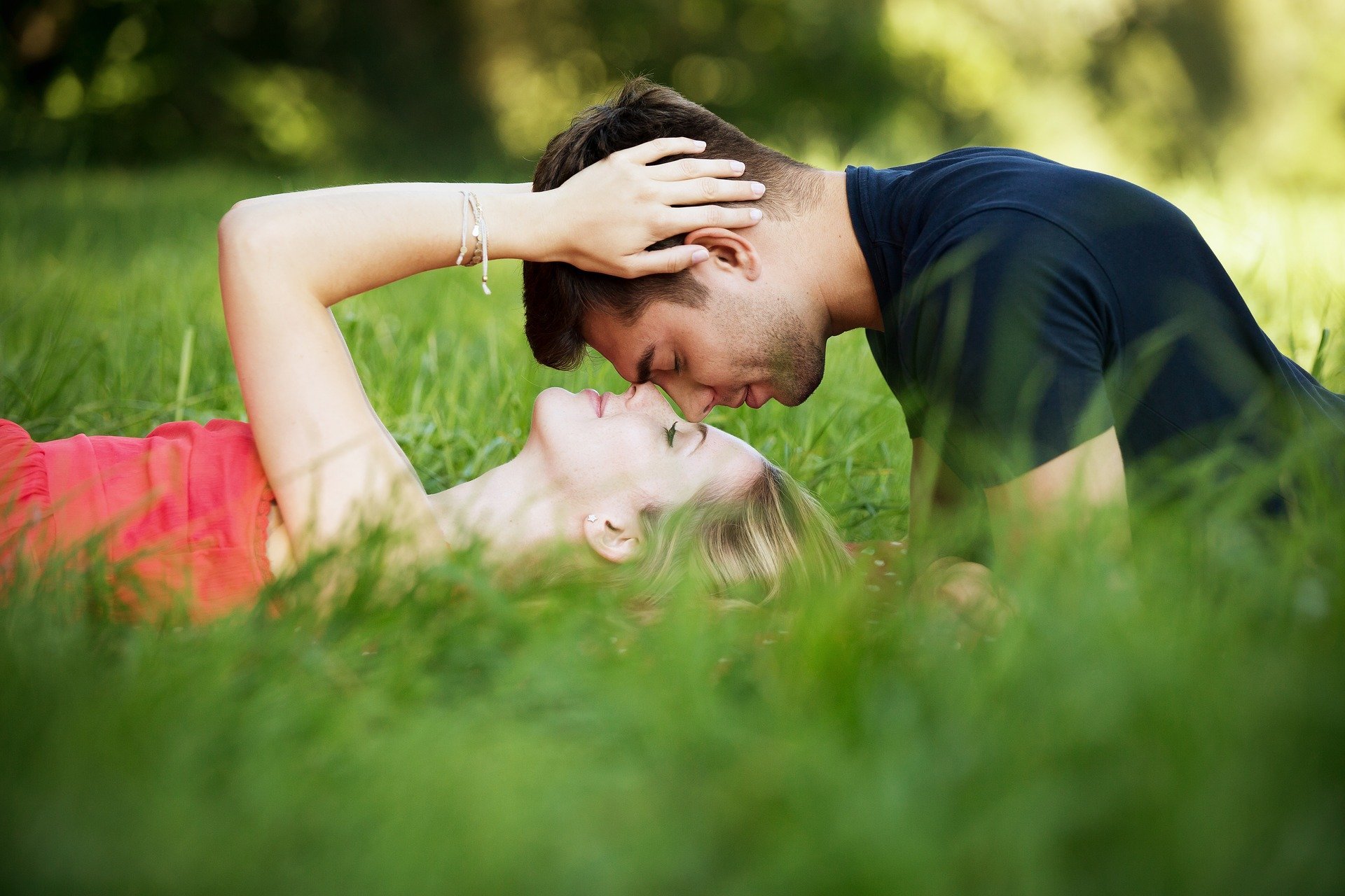 Mulher beijando testa de homem enquanto os dois estão deitados na grama