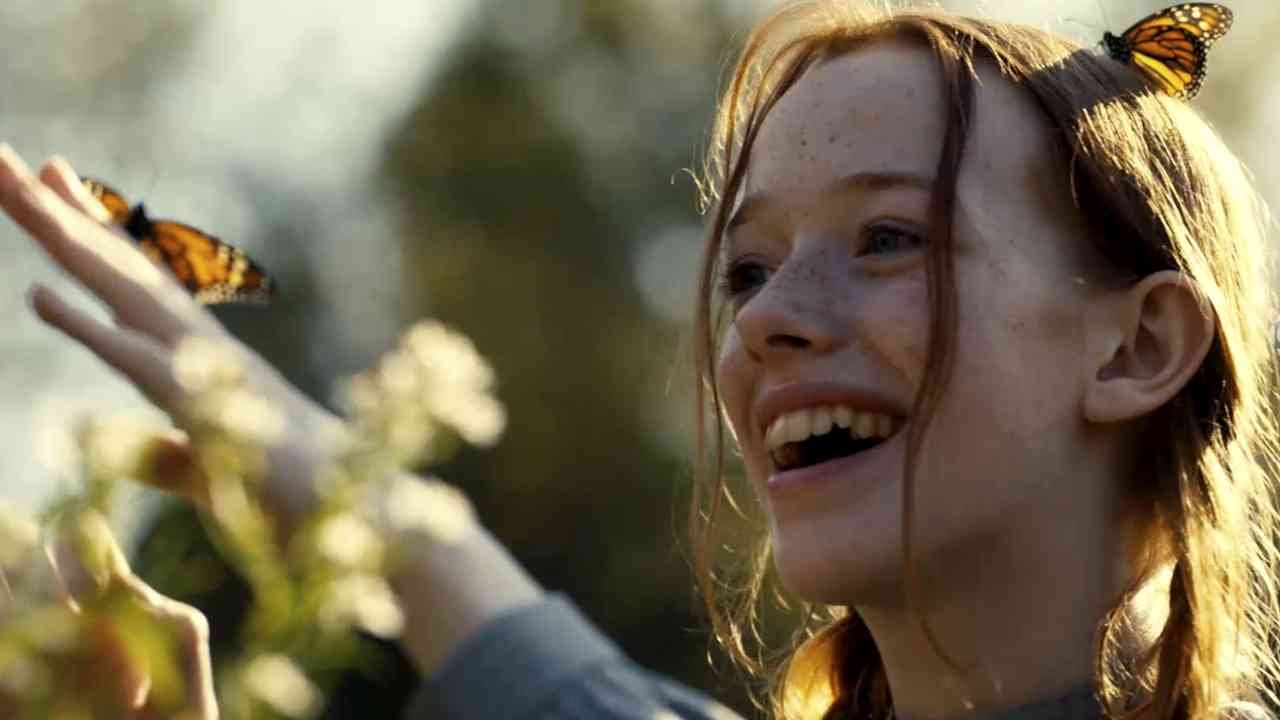 Personagem da série  Anne with an E sorridente brincando com borboletas em campo