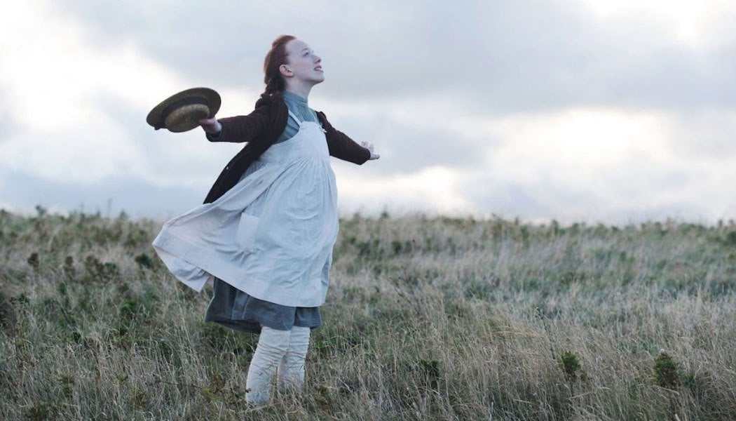 Personagem da série Anne with an E com os braços abertos sentindo o vento em uma plantação de trigo