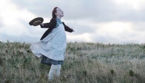 Reprodução/ Mix de séries Personagem da série Anne with an E com os braços abertos sentindo o vento em uma plantação de trigo