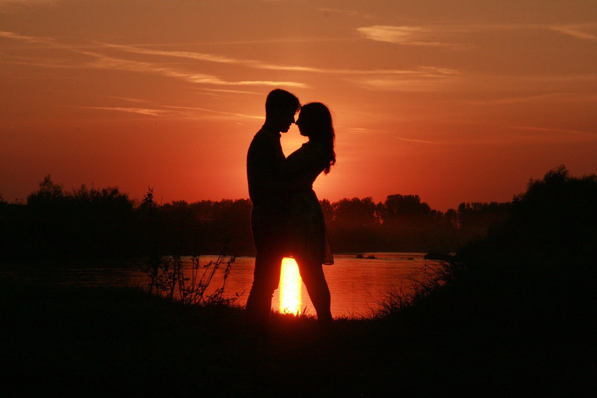 Silhueta de casal frente à frente em pôr do sol perto de lago