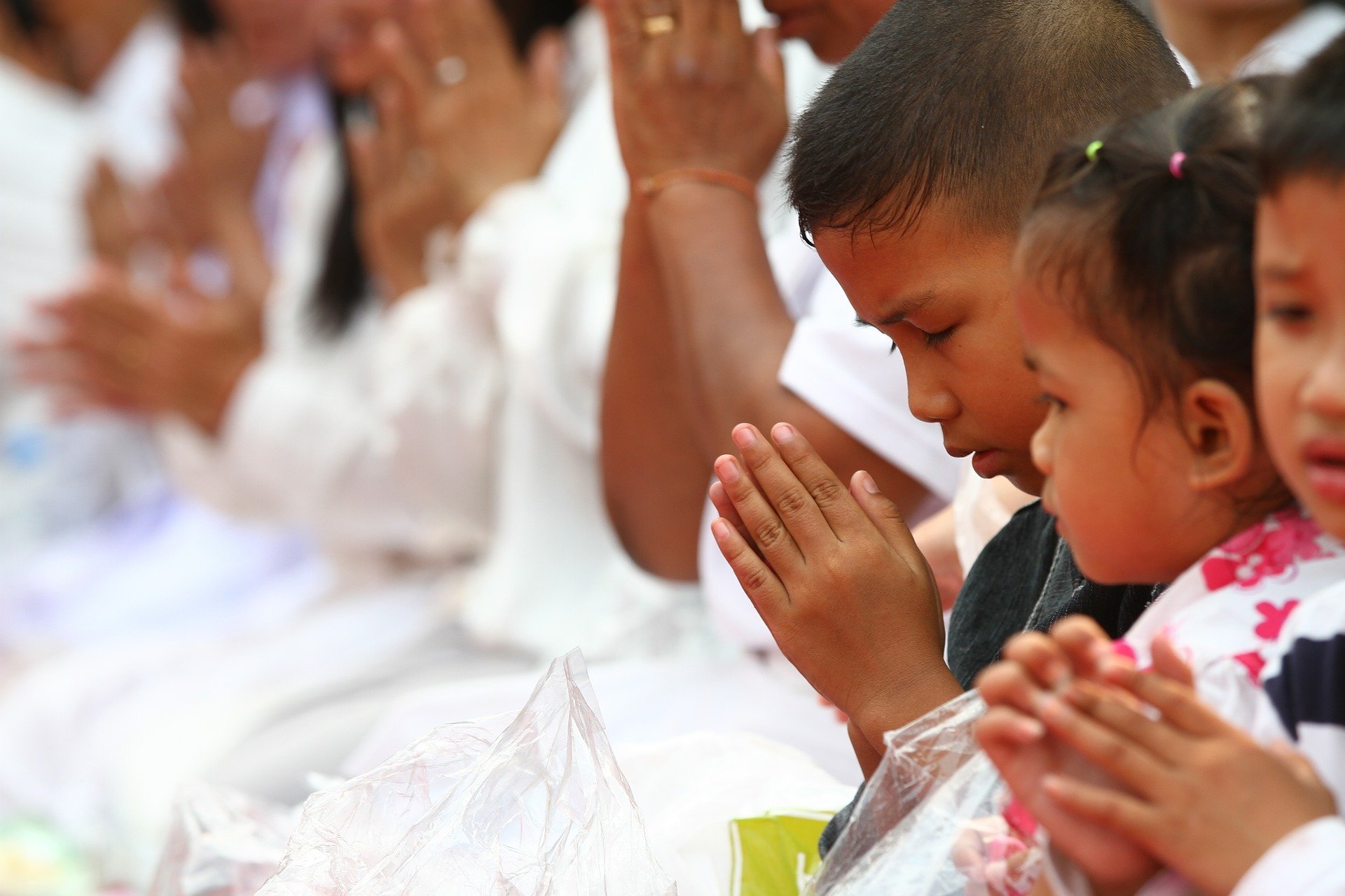 Grupo de pessoas vestindo branco, todas com as mãos unidas em sinal de oração