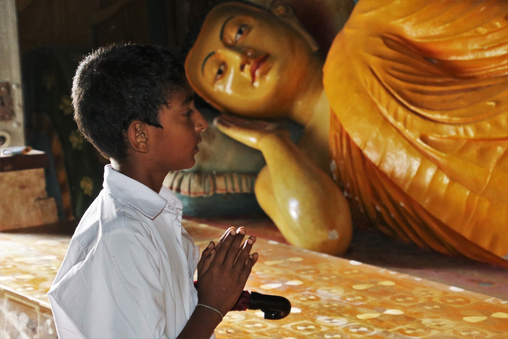 Menino com as mãos unidas orando próximo de estátua hindu