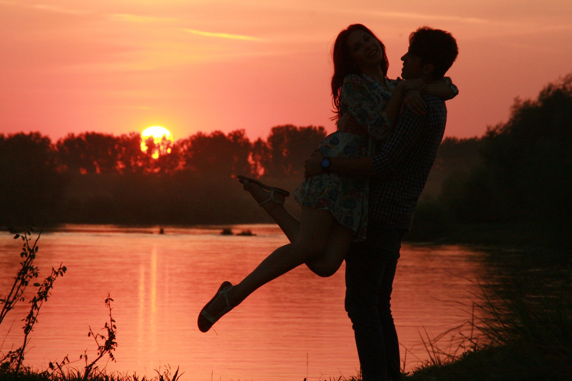 Homem e mulher se abraçando perto de lago, ao pôr do sol