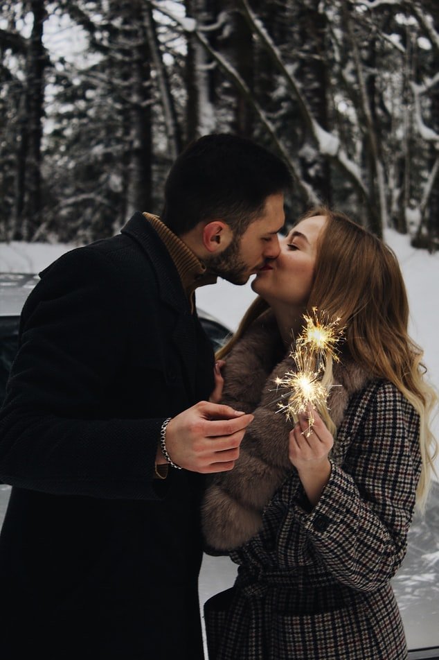 Casal se beijando em floresta cheia de neve