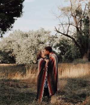 Unsplash Homem e mulher se beijando enrolados em manta no meio da natureza