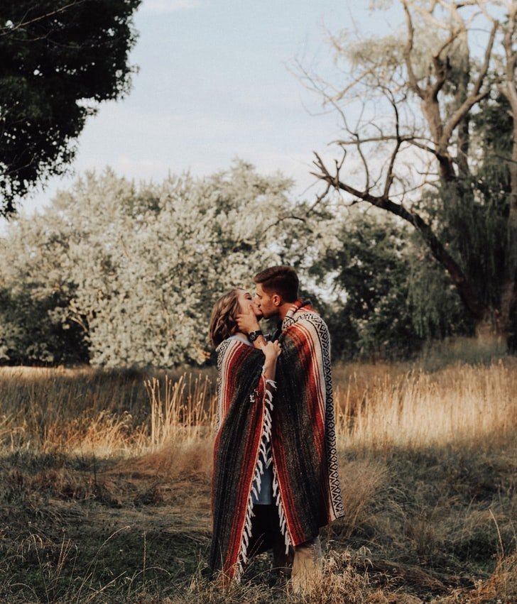 Homem e mulher se beijando enrolados em manta no meio da natureza