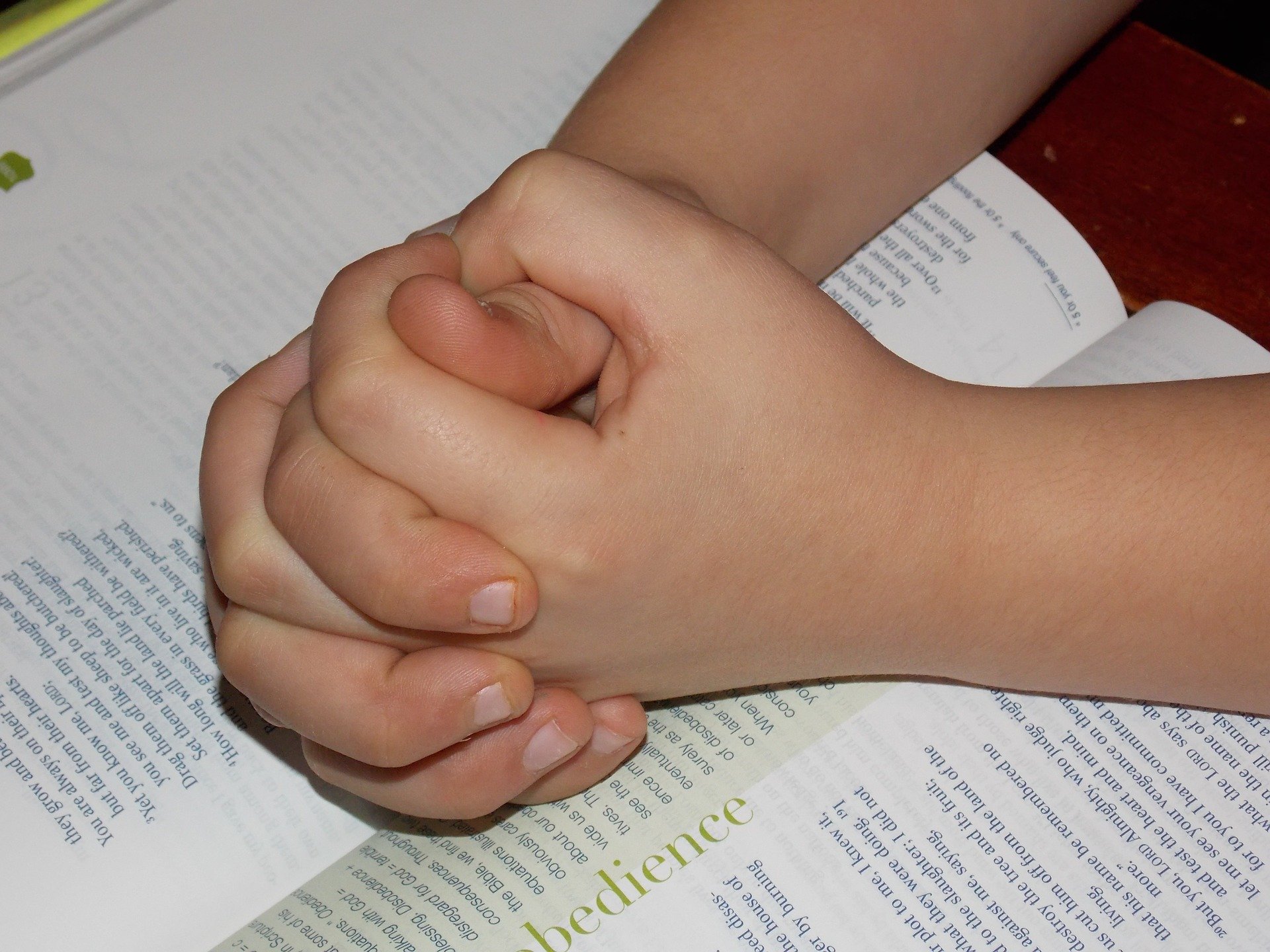 Mãos de criança unida apoiadas em cima de bíblia, em sinal de oração