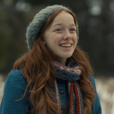 Personagem principal da série Anne with an E sorrindo em bosque enquanto neva