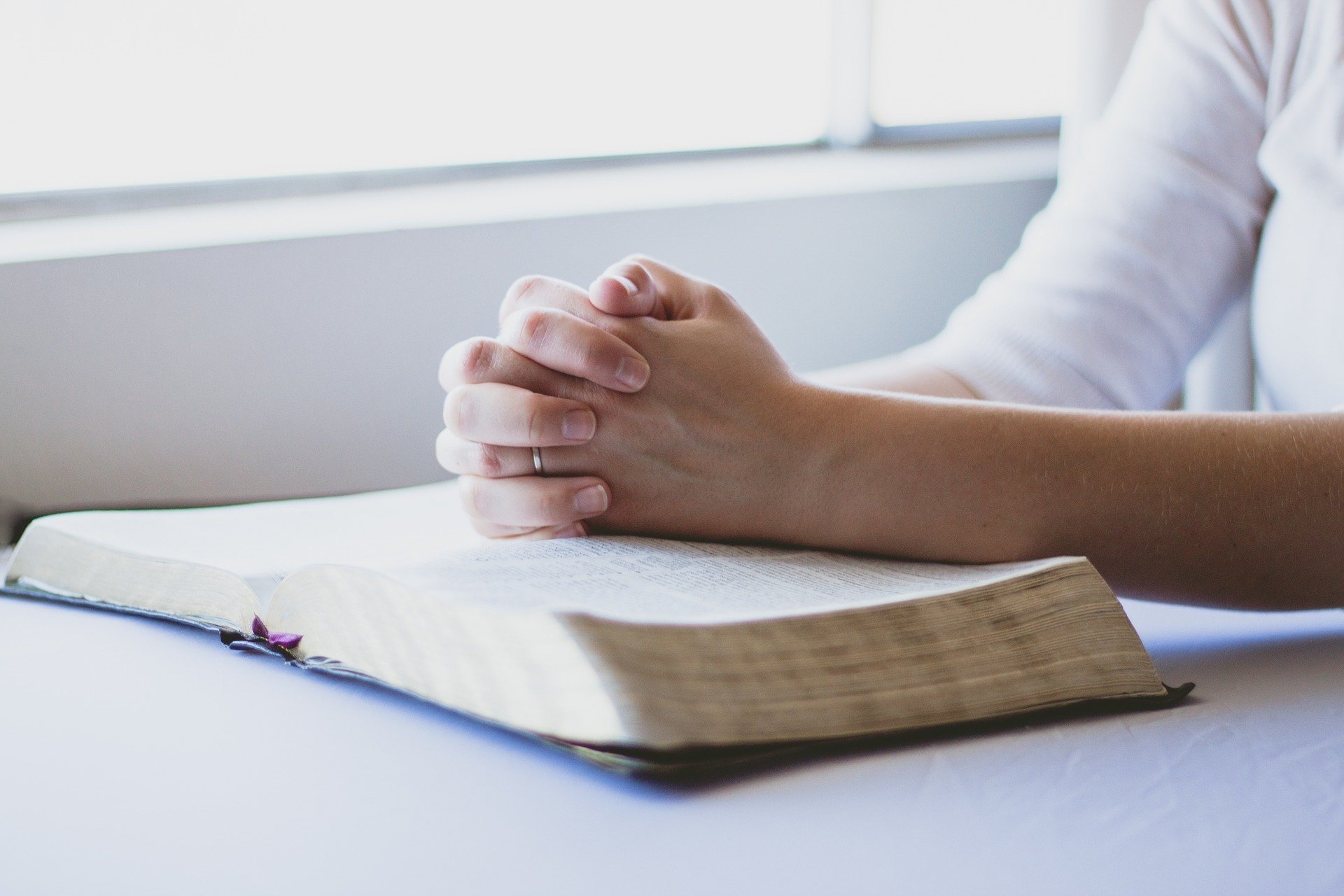 Mulher orando com as mãos apoiadas sobre a bíblia