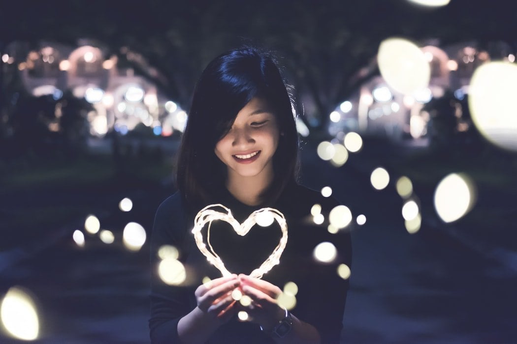 Mulher sorrindo segurando fio de luzes em formato de coração