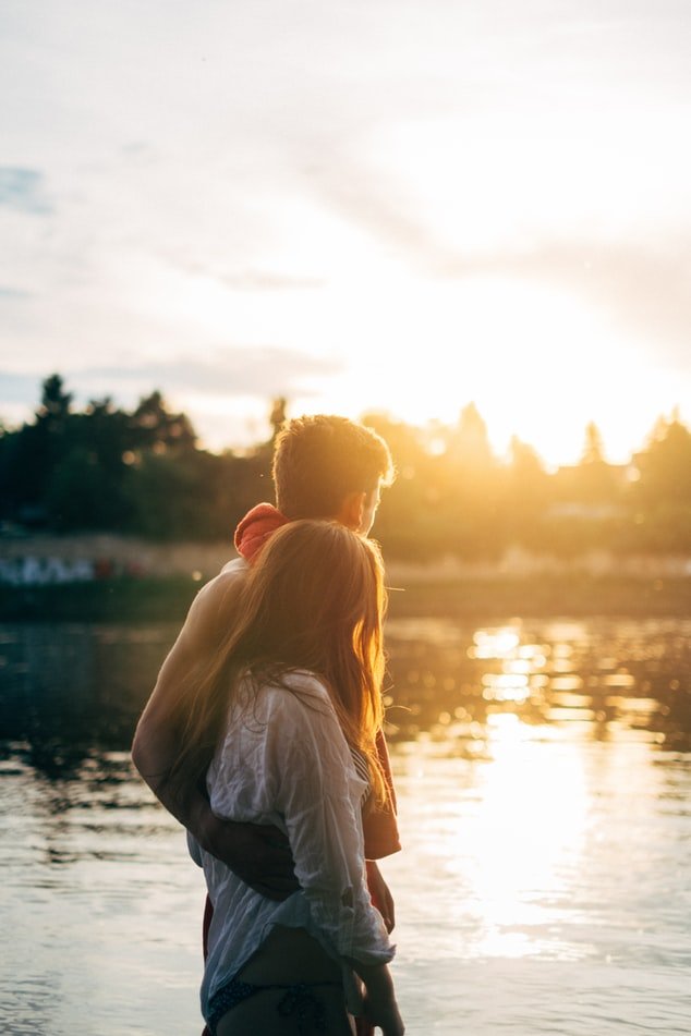 Casal abraçados observando pôr do sol em lago