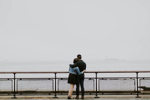 Casal abraçados observando paisagem nublada de mar