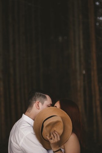 Homem e mulher beijando-se com chapéu em frente ao rosto de ambos