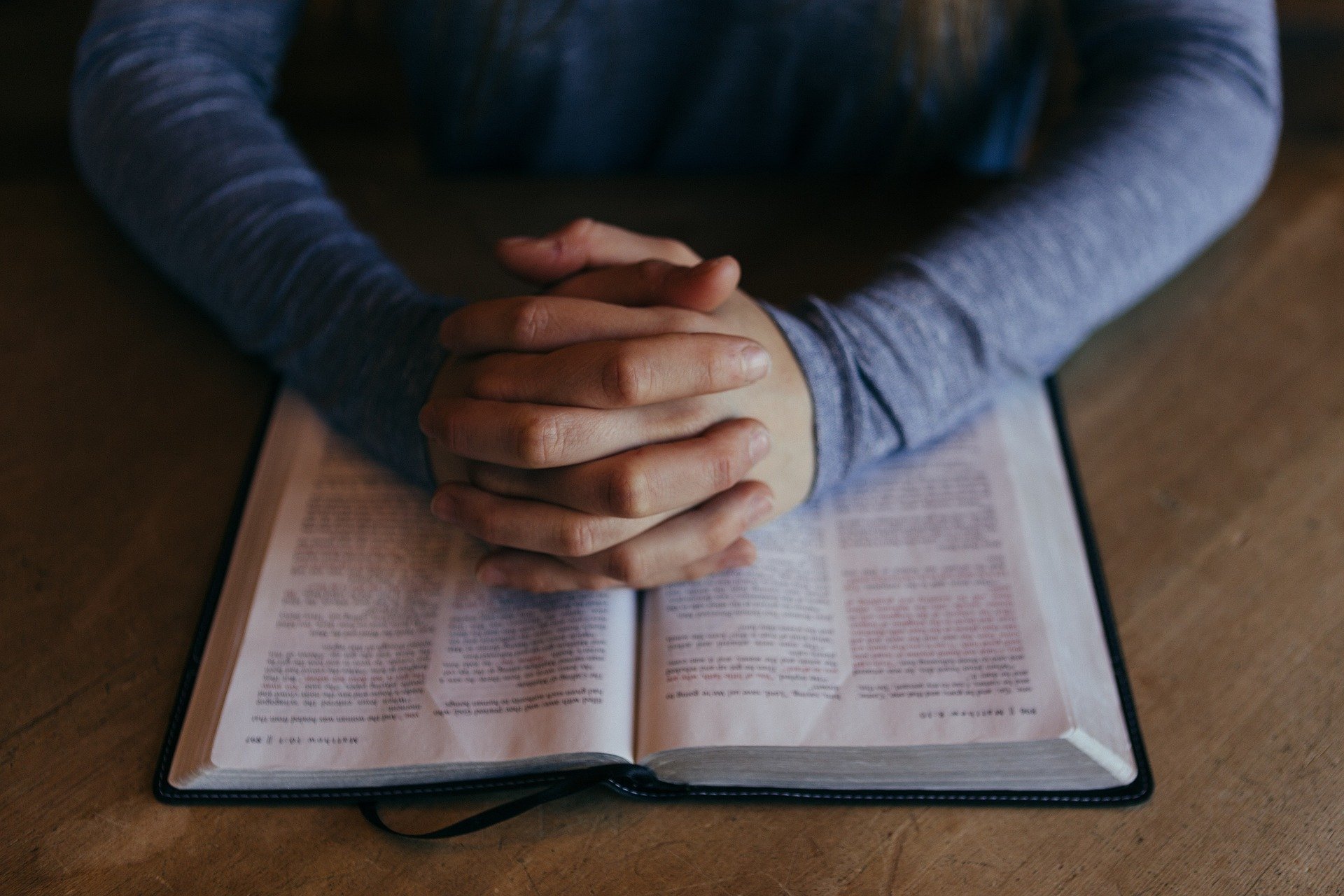 Homem orando com as mãos apoiadas em bíblia aberta