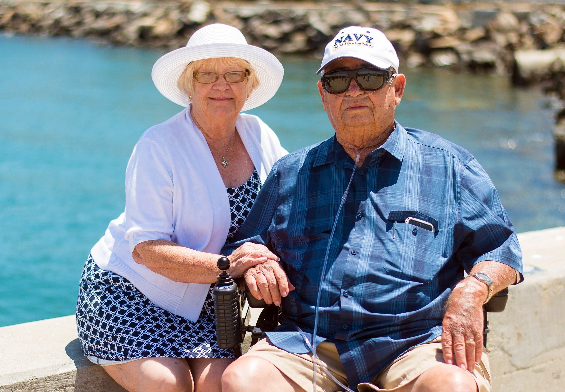 Casal de idosos posando para foto sentados perto de lago