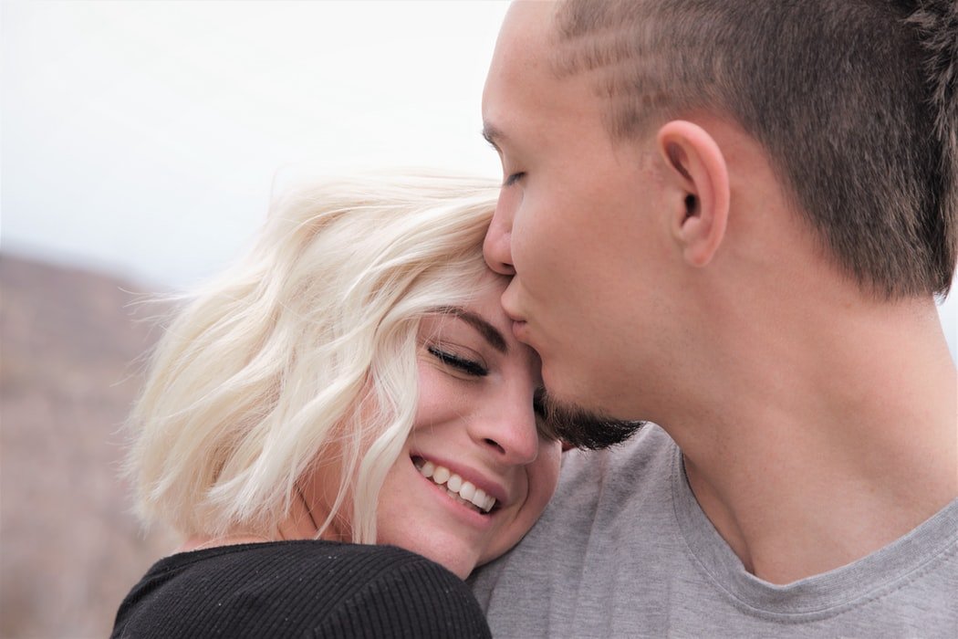 Homem beijando testa de mulher sorrindo