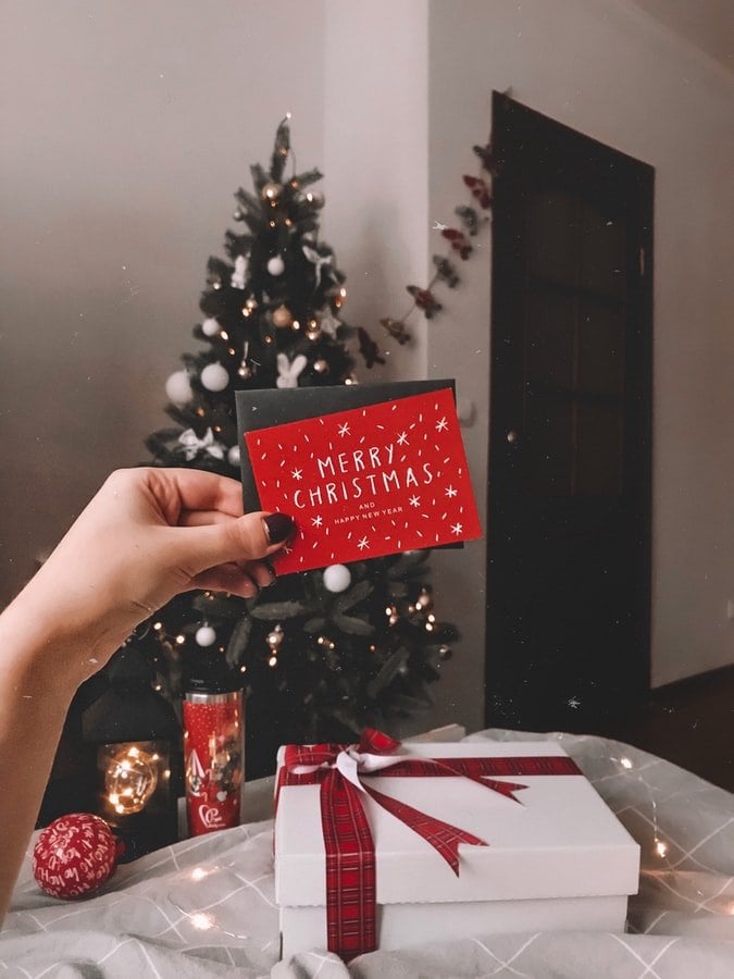 Mão de pessoa segurando cartão natalino perto de caixa de presente