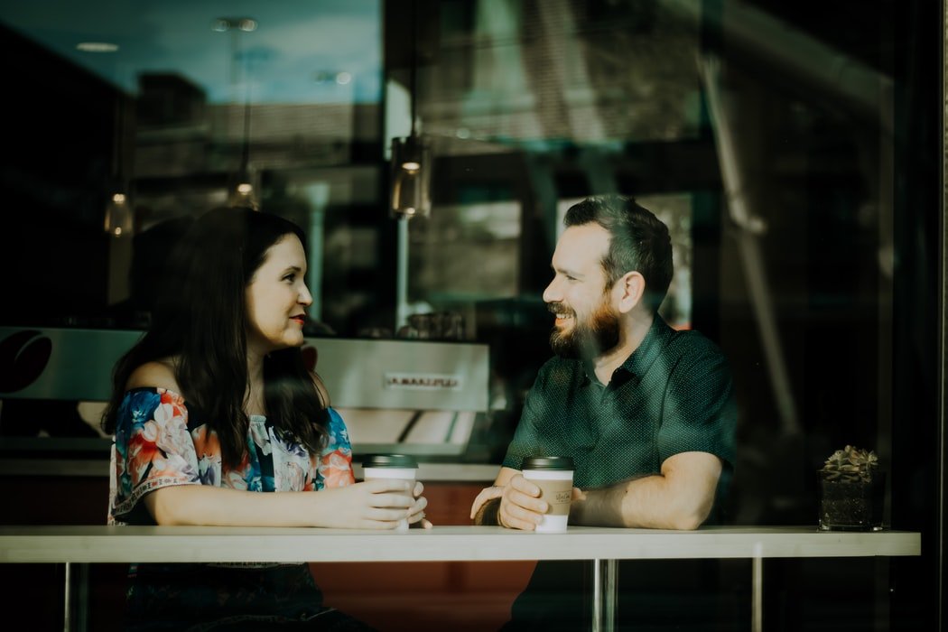 Homem e mulher sentados em mesa de café, olhando um para outro