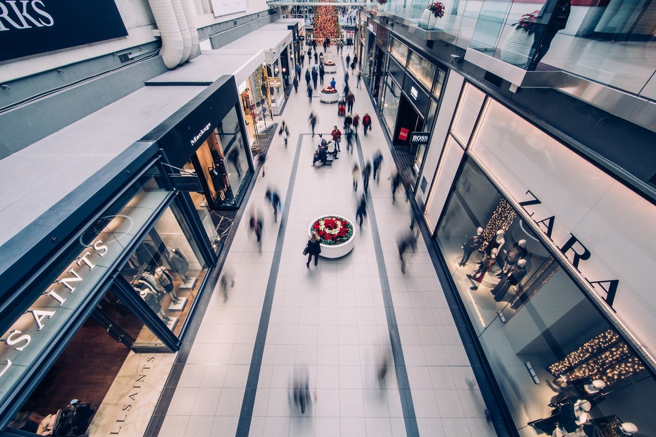 Foto de corredor de shopping, visto de um mezanino ou segundo andar, com pessoas andando.