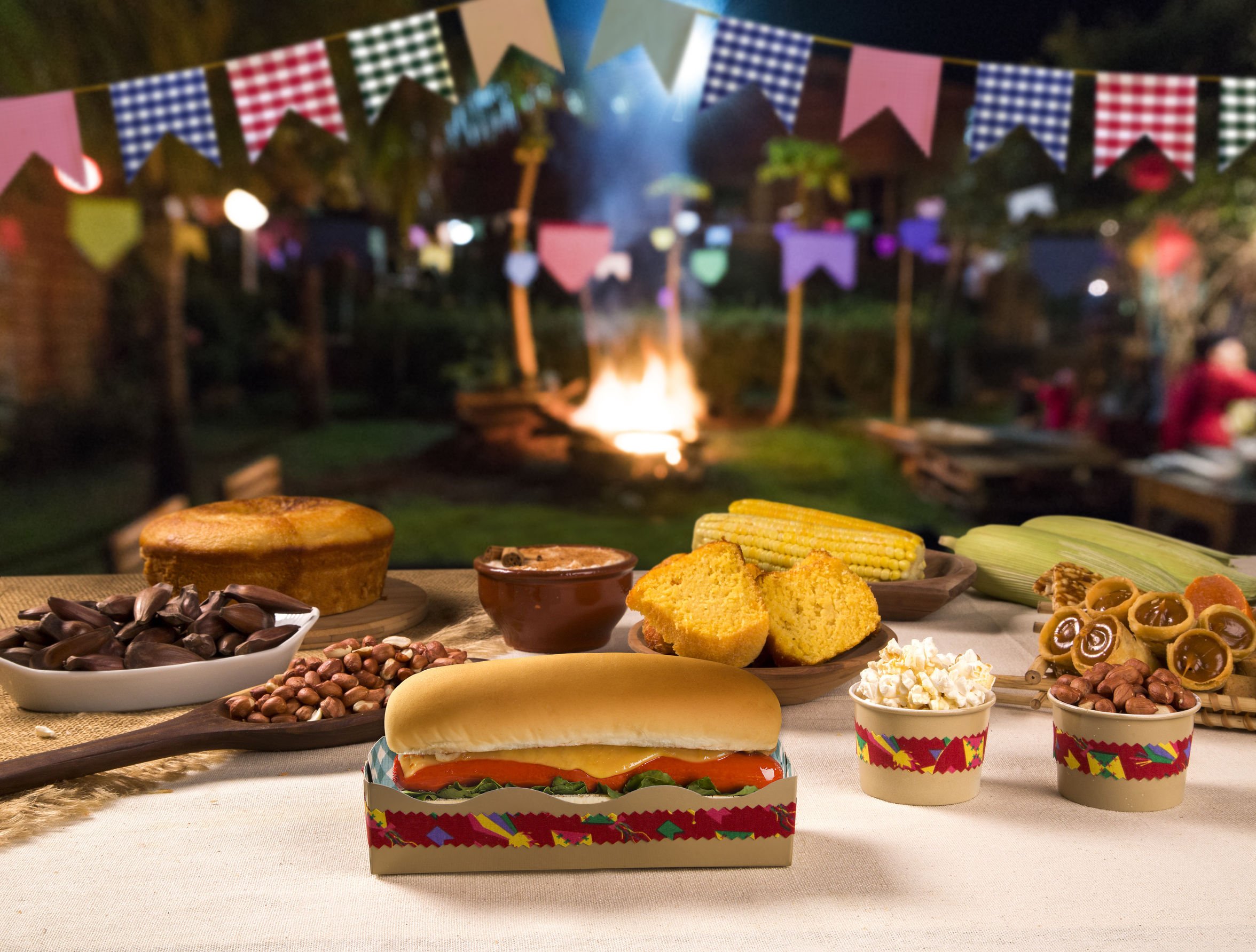 Festa junina com bandeirinhas e uma mesa com hotdog, pipoca, doces