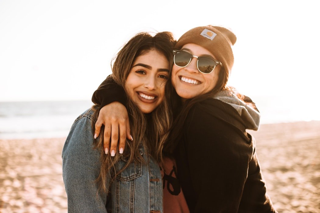 Duas mulheres jovens se abraçando enquanto posam para foto em praia