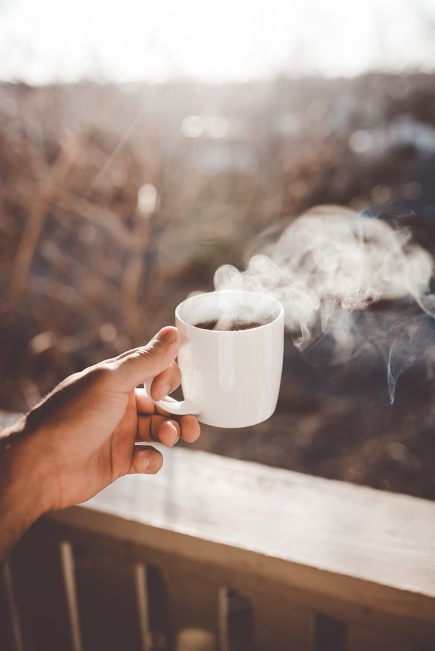 Mão segurando xícara de café e nascer do sol ao fundo