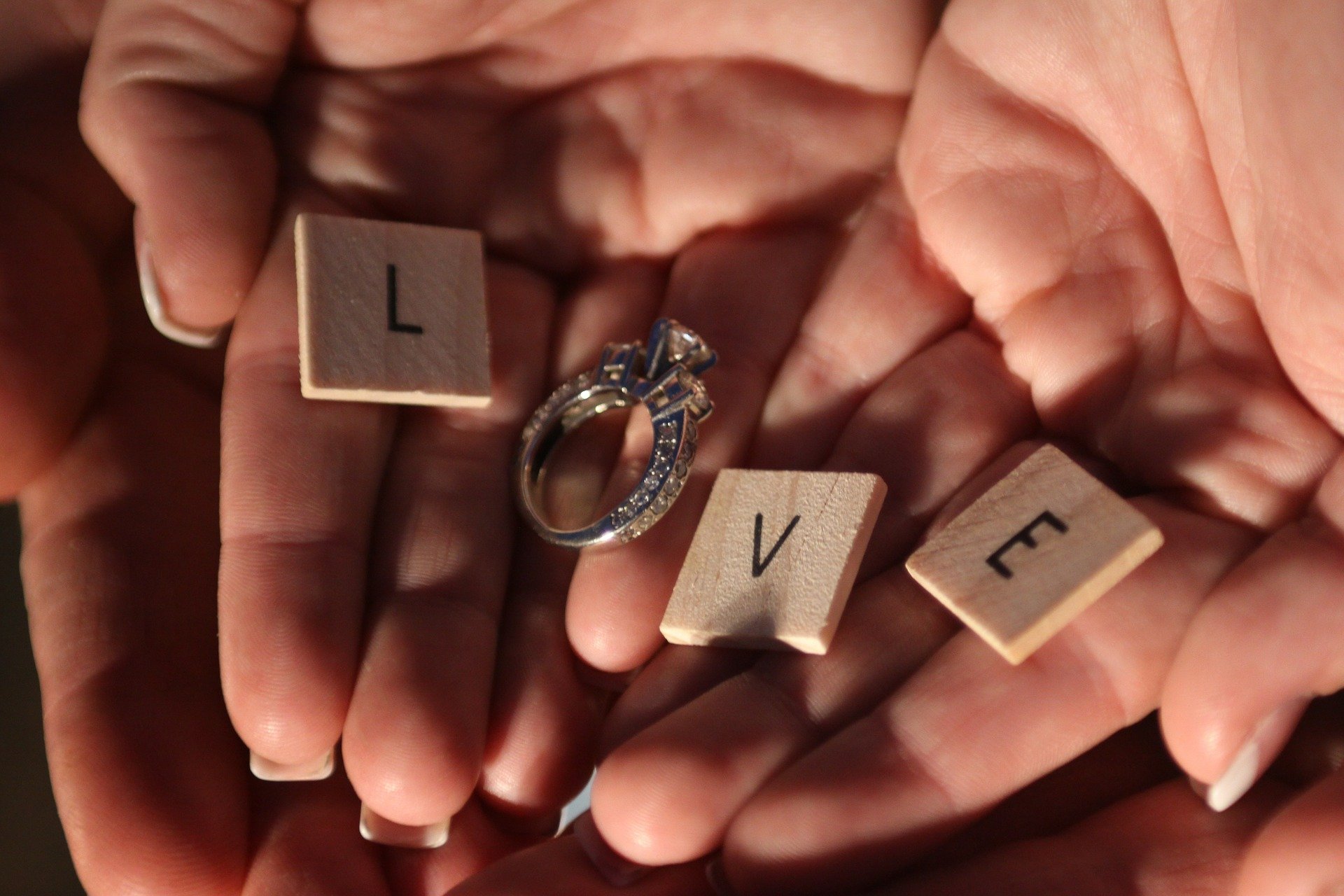 Mãos de casal de noivos segurando aliança de noivado e letras de madeira formando a palavra amor escrito em inglês