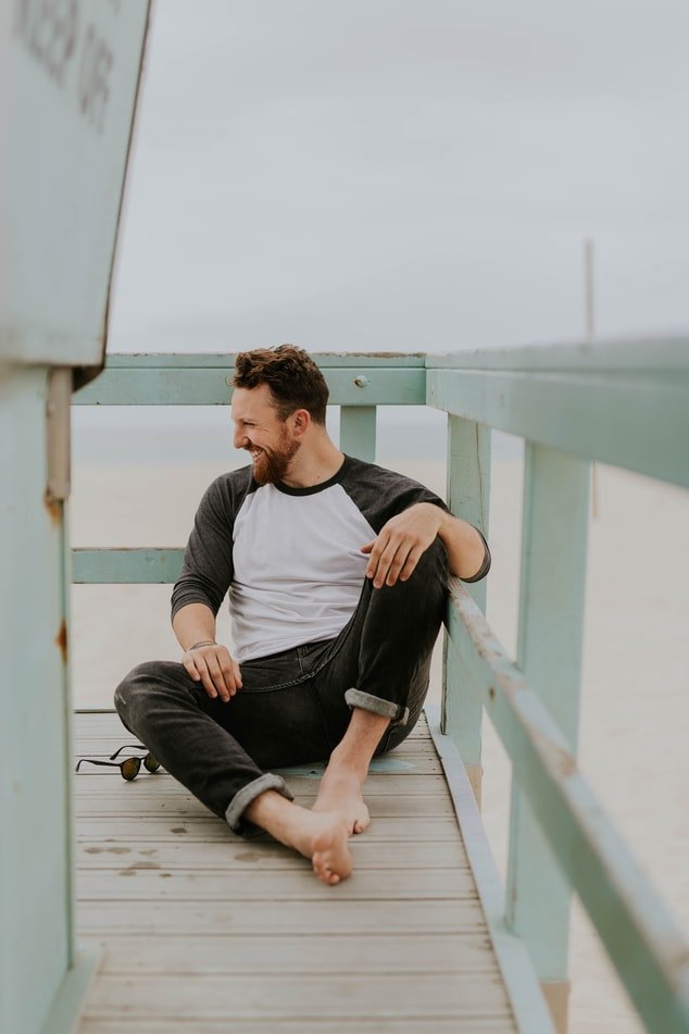 Homem sentado em pier de praia, dando risada