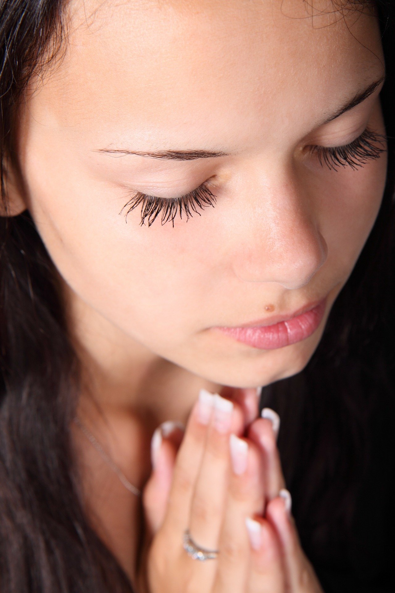 Mulher orando com as mãos unidas e olhos fechados