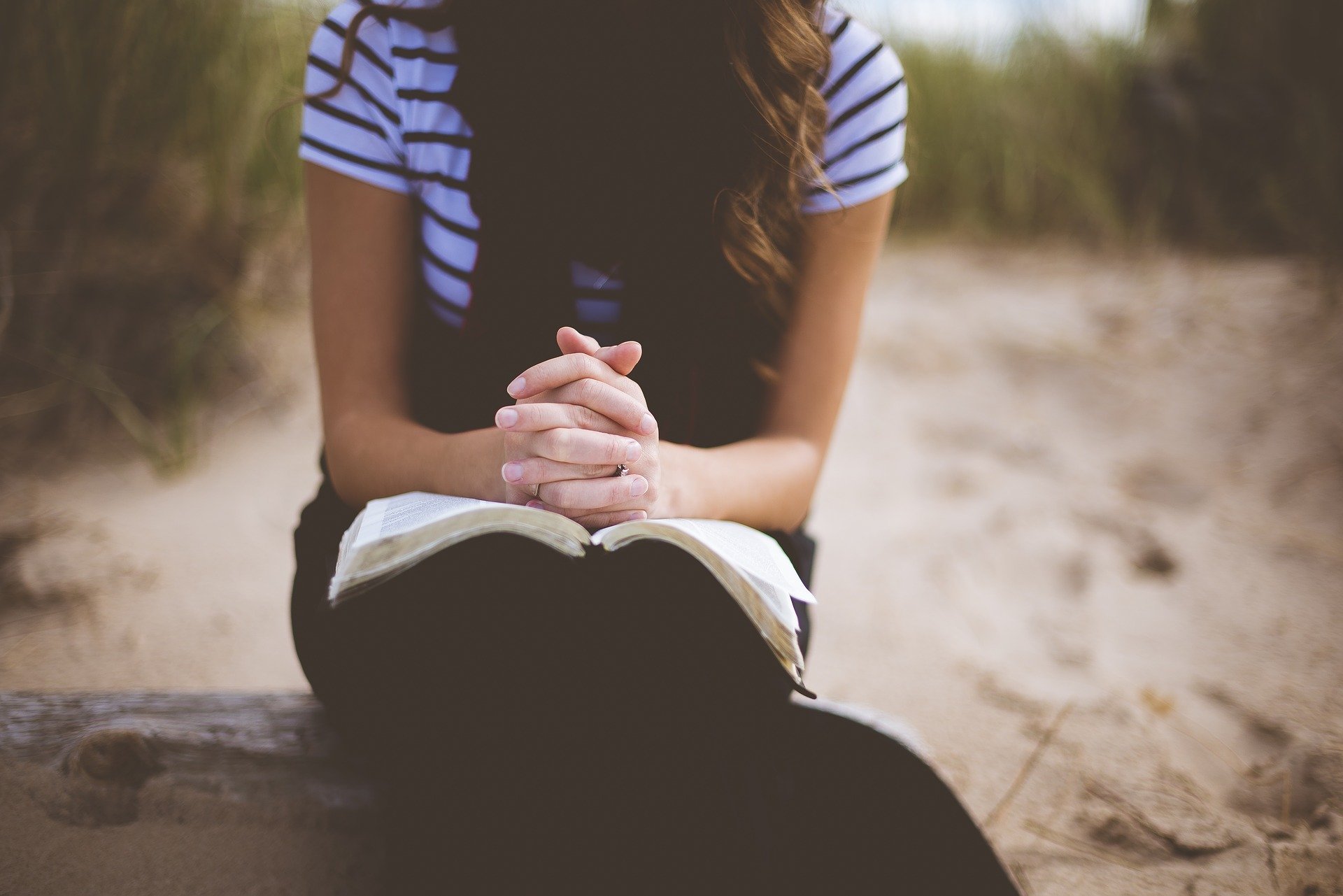 Mulher orando com as mãos apoiadas sobre a bíblia aberta sentada no chão