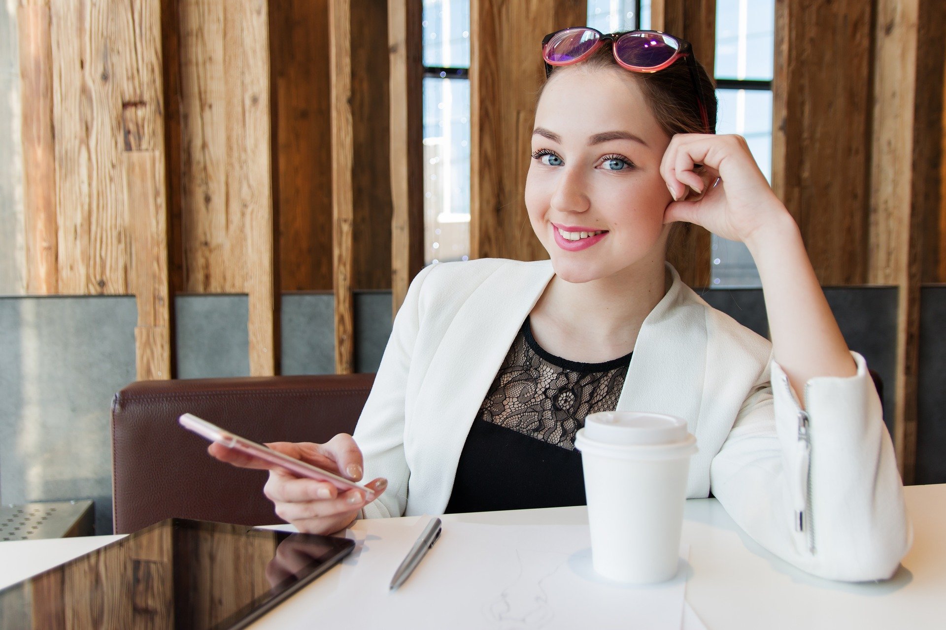 Mulher sentada em mesa de restaurante, sorrindo e mexendo no celular
