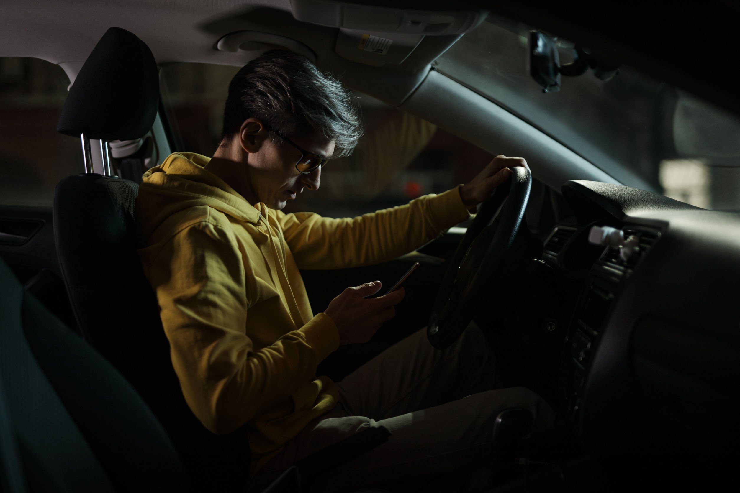 Anton Horobets /123RF Homem dentro de carro, a noite, mexendo em celular