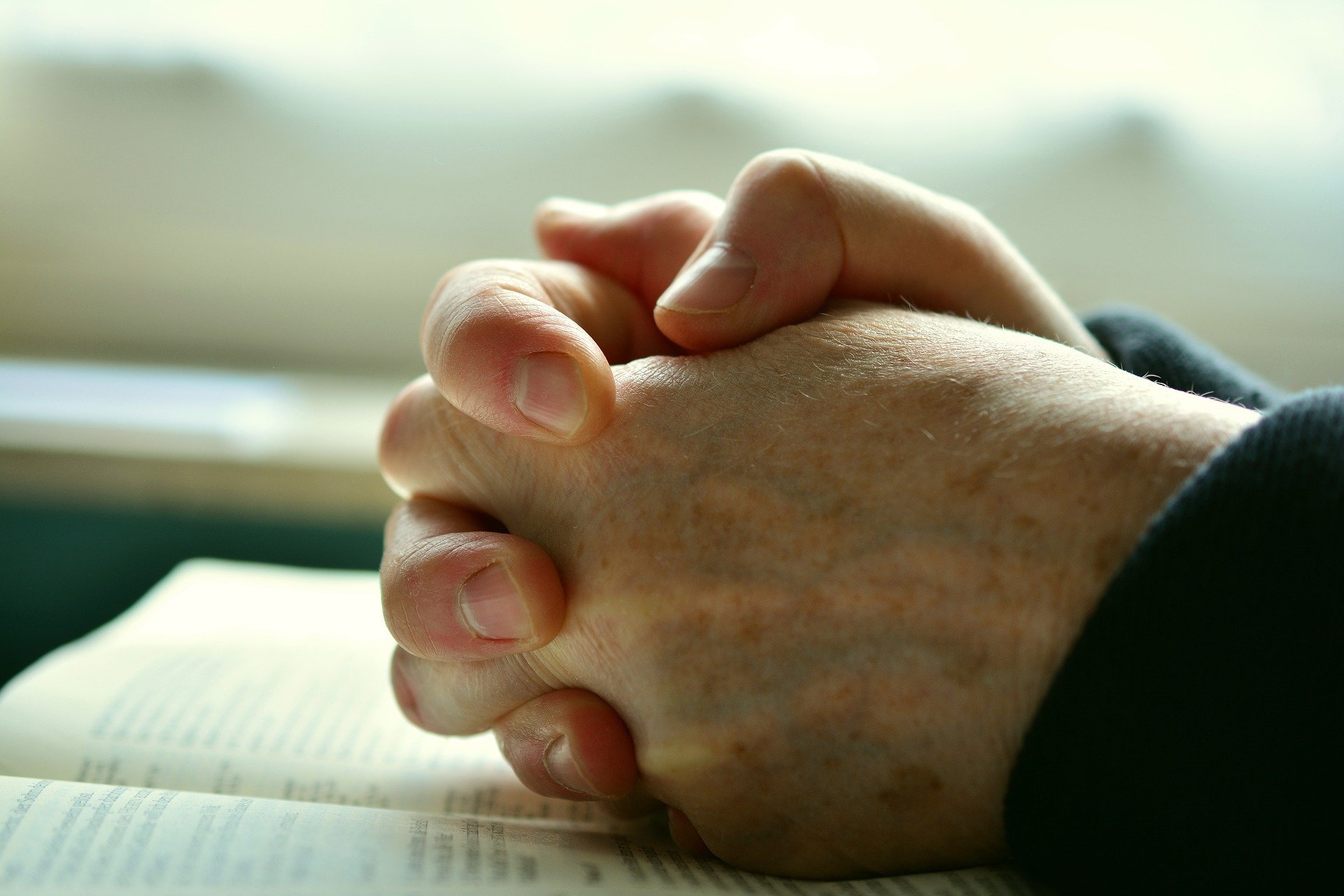 Mão de pessoa apoiadas sobre a bíblia orando