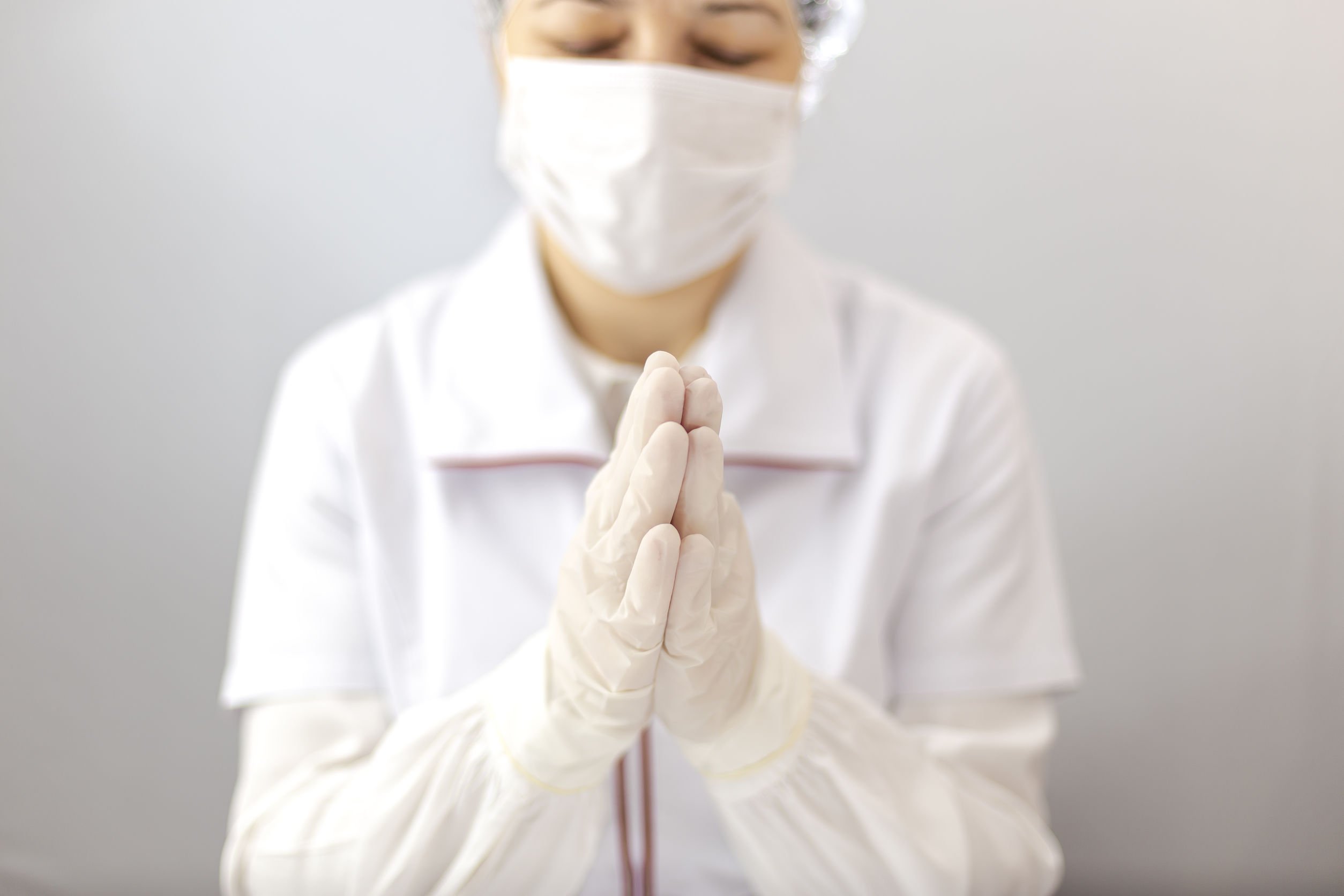 Médica usando touca, luvas e máscara, com as mãos unidas, orando