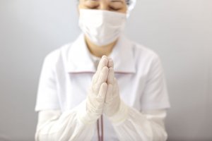 bymandesigns / 123RF Médica usando touca, luvas e máscara, com as mãos unidas, orando