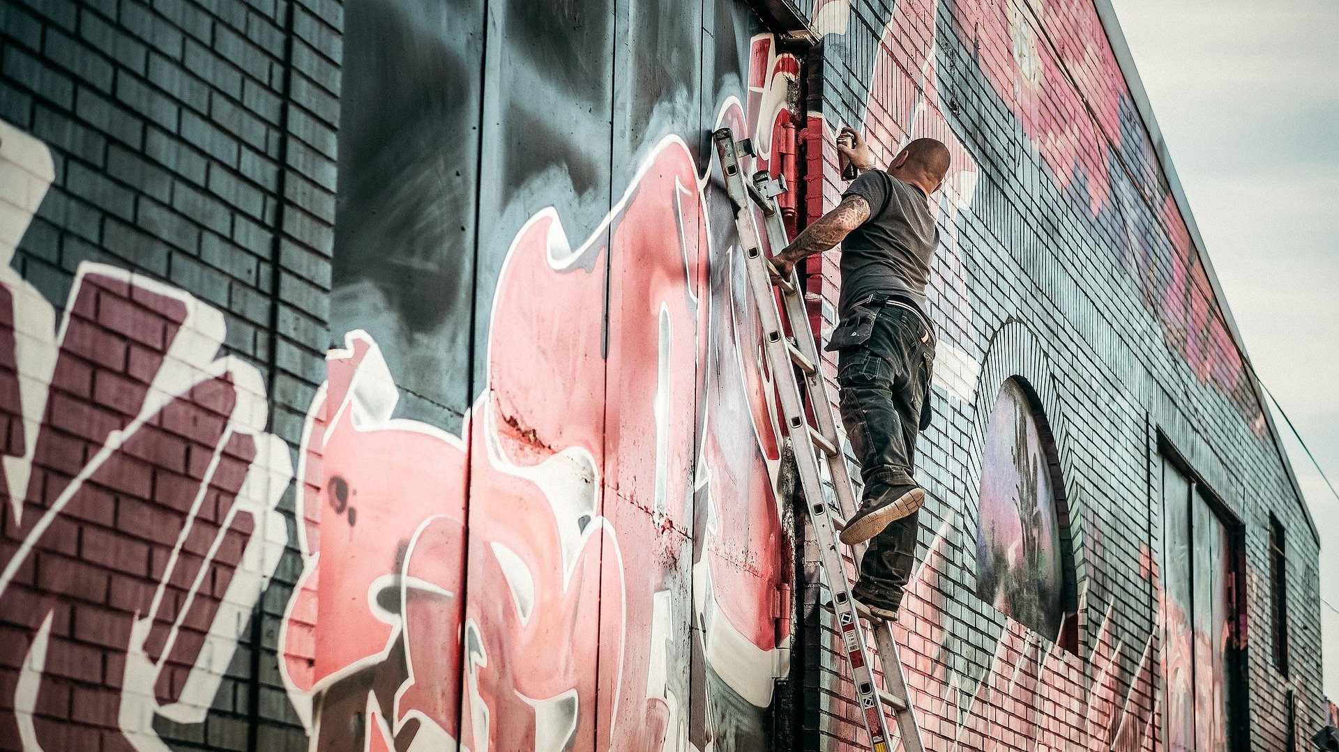 Homem em pé em escada, grafitando muro